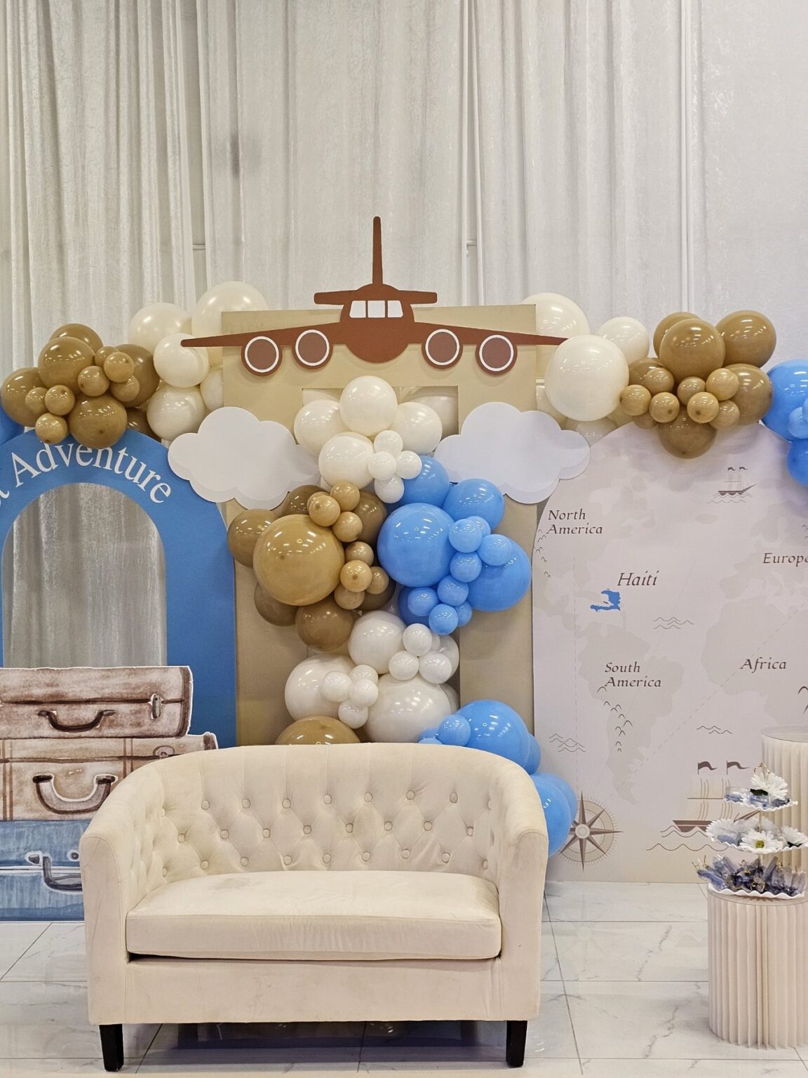 Adventure themed baby shower backdrop with an ivory loveseat