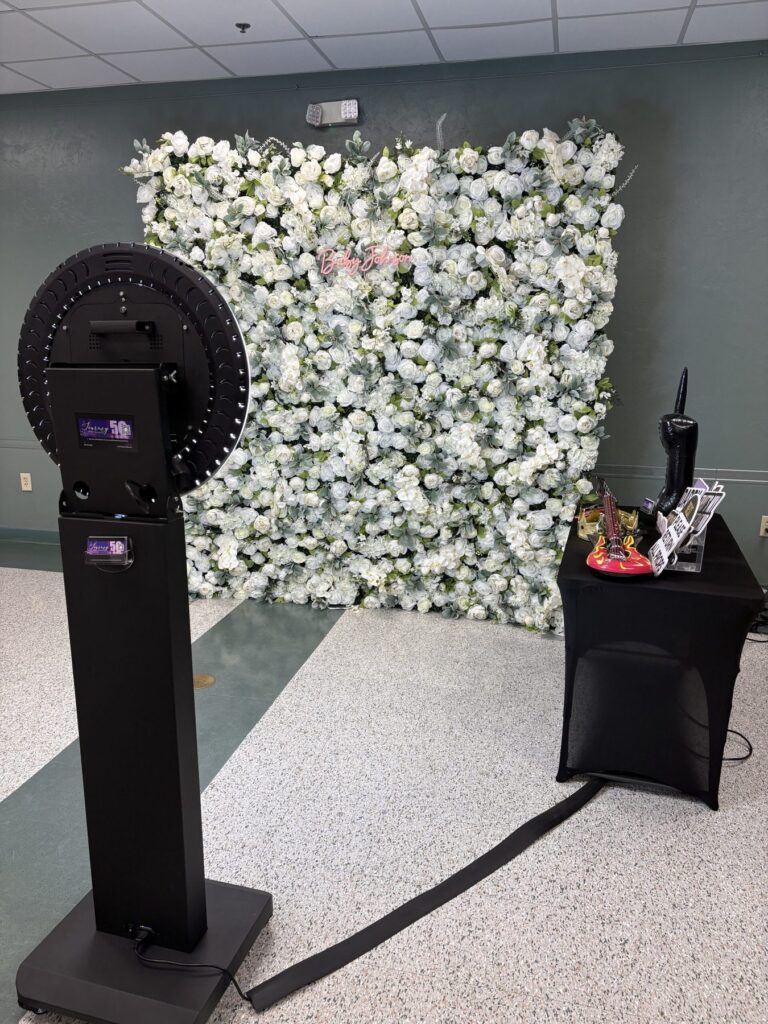 Selfie photo booth set up beside a white flower wall at an event
