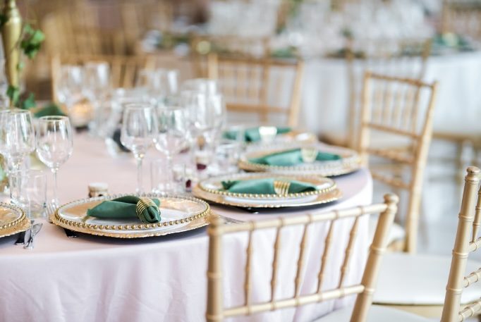 Round tables set with green napkins, gold chargers and gold chiavari chairs