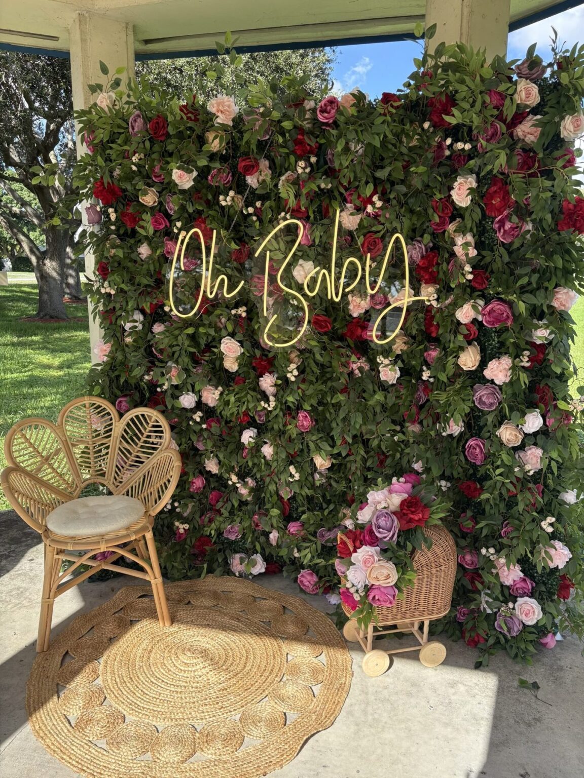 Rose garden flower wall with an Oh Baby neon sign, rattan chair and round jute rug